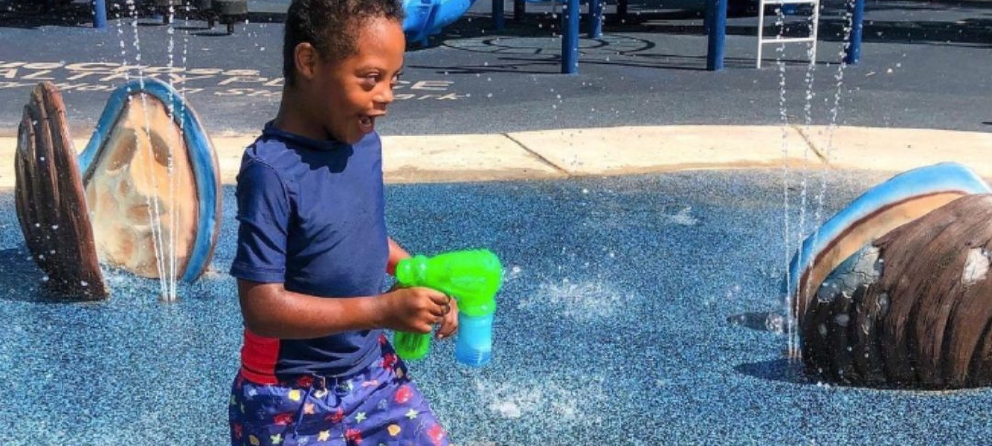 Young boy playing with water at a colorful splash pad playground.