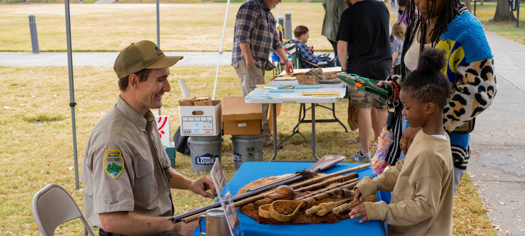 Park ranger showing animal hides to children at an outdoor educational booth.