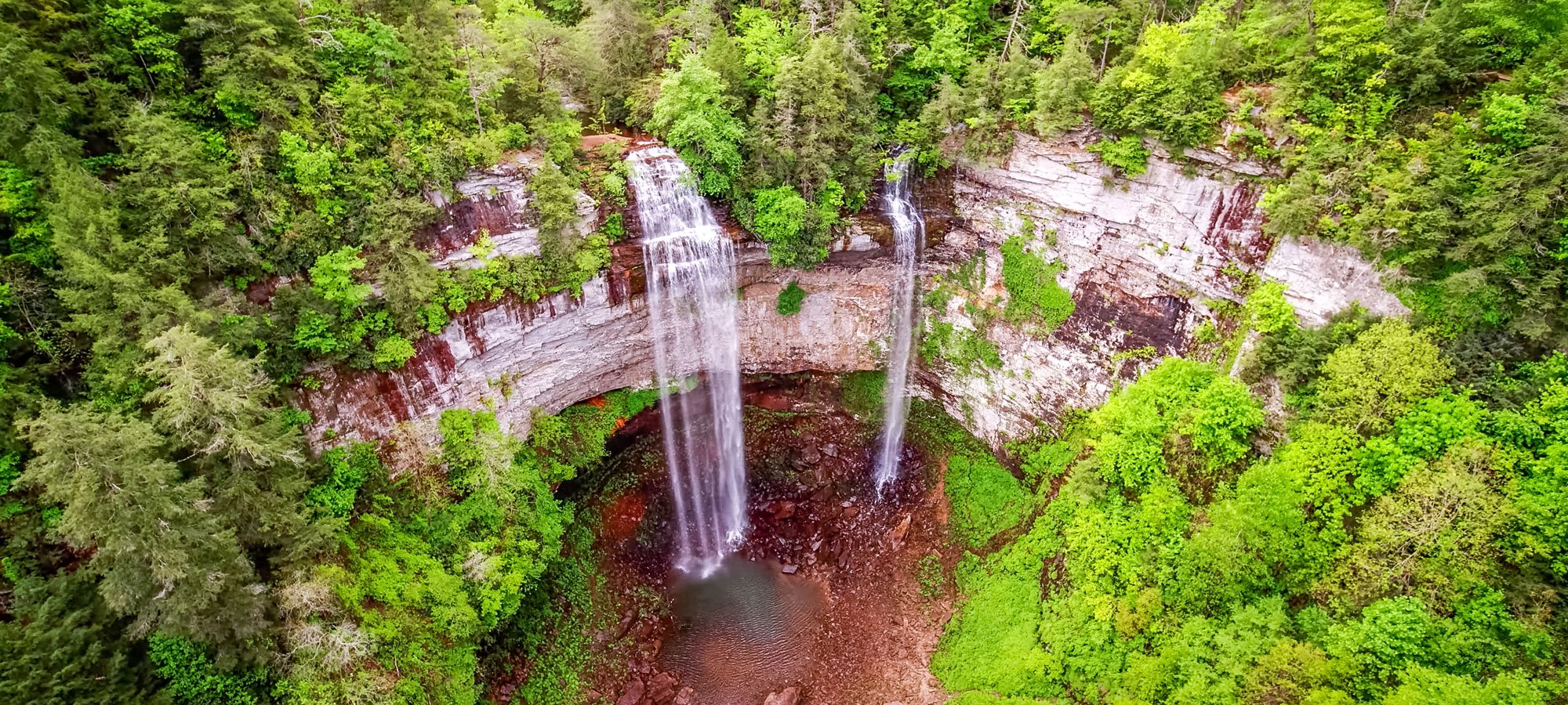 Fall Creek Falls waterfall drops over a rock ledge into a small pool surrounded by green trees