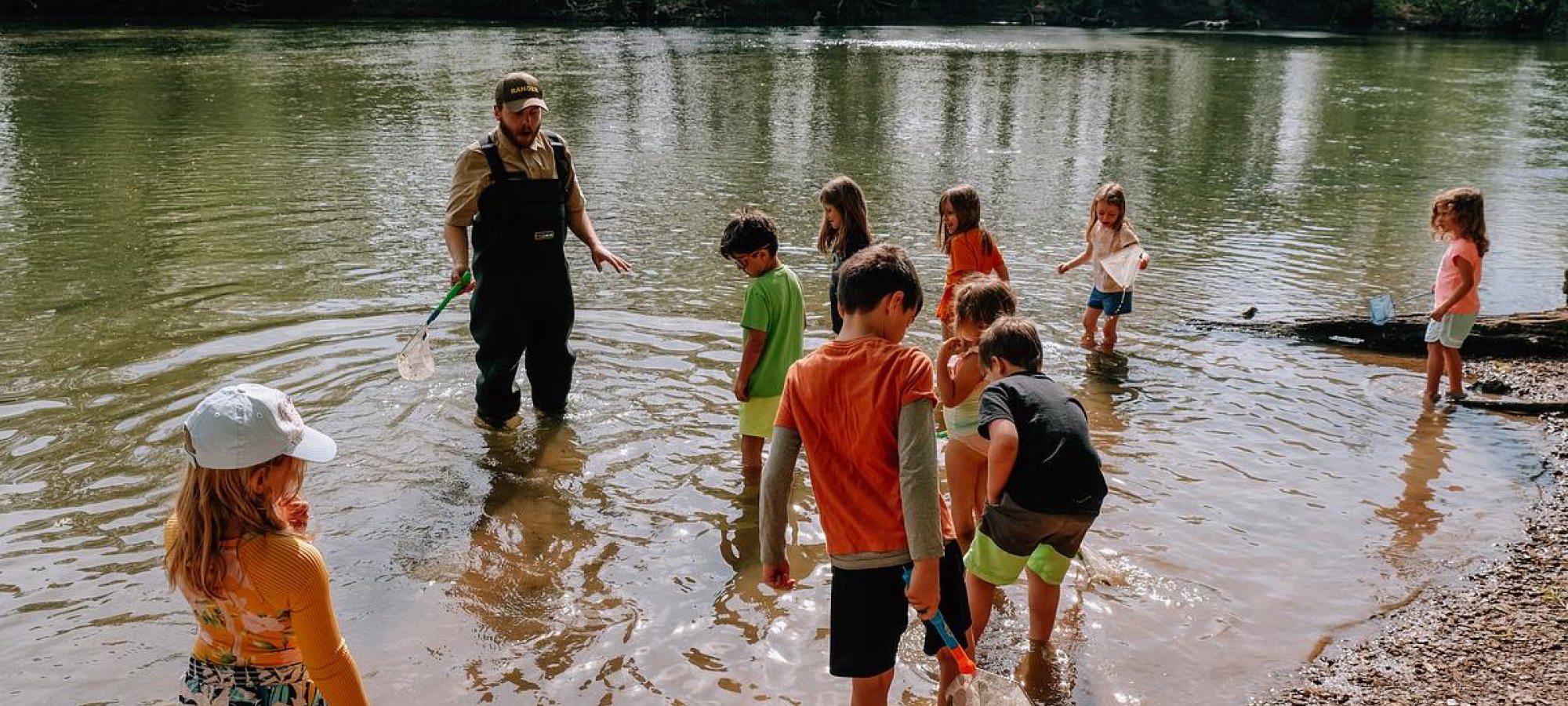 Group of children and adult cleaning riverbank on sunny day.