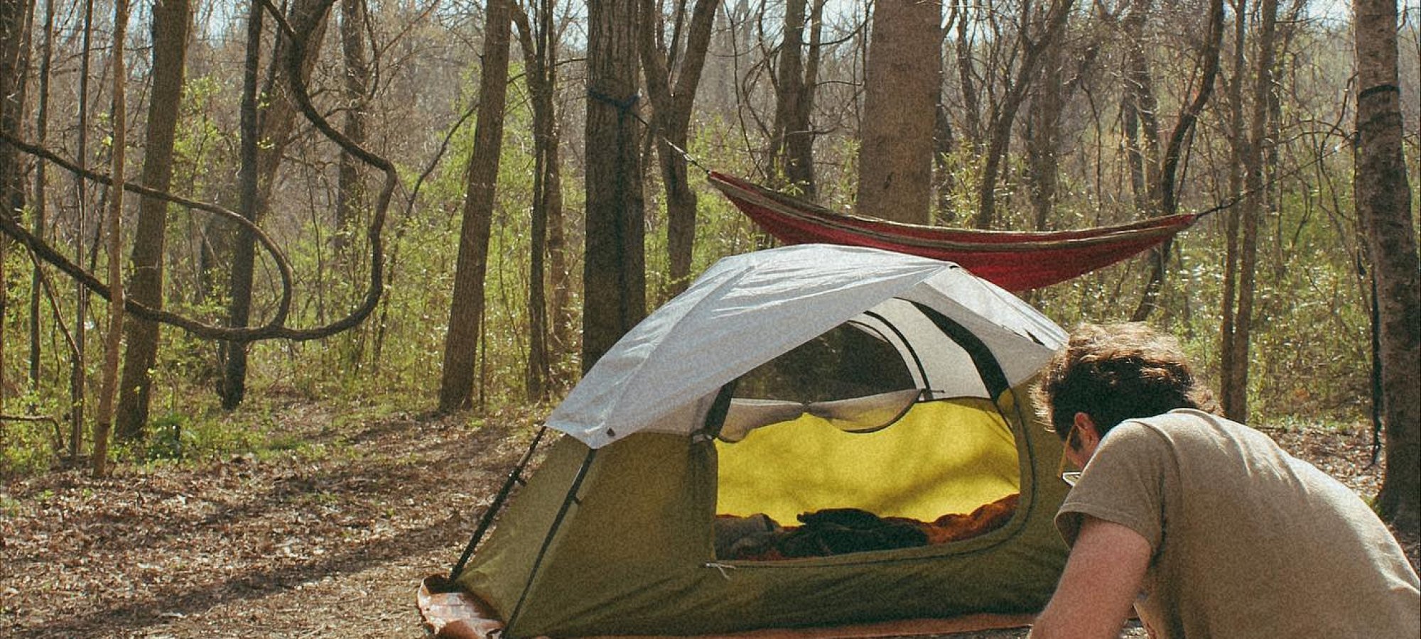 Person setting up a campfire near a tent in a forest.