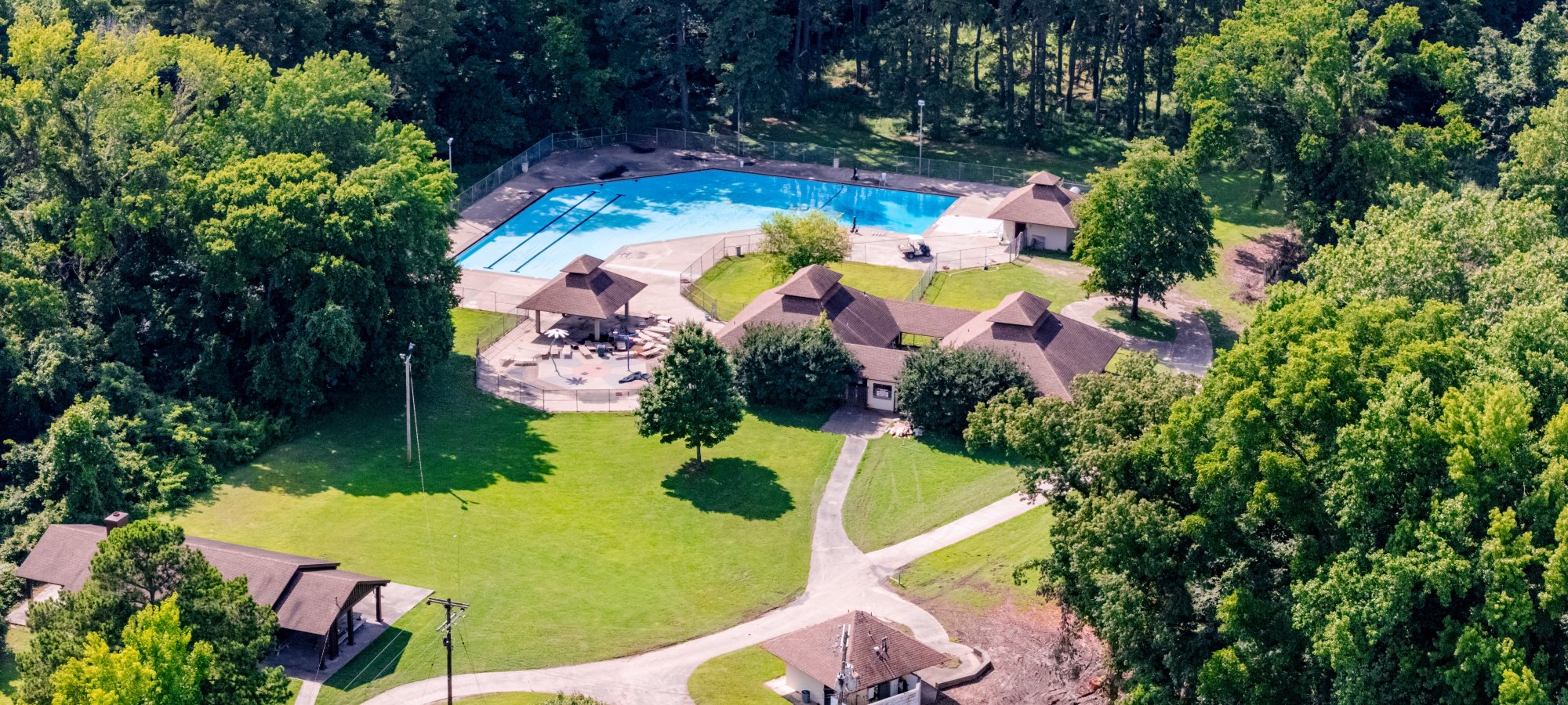 Aerial view of park with outdoor pool, surrounded by trees and small buildings.