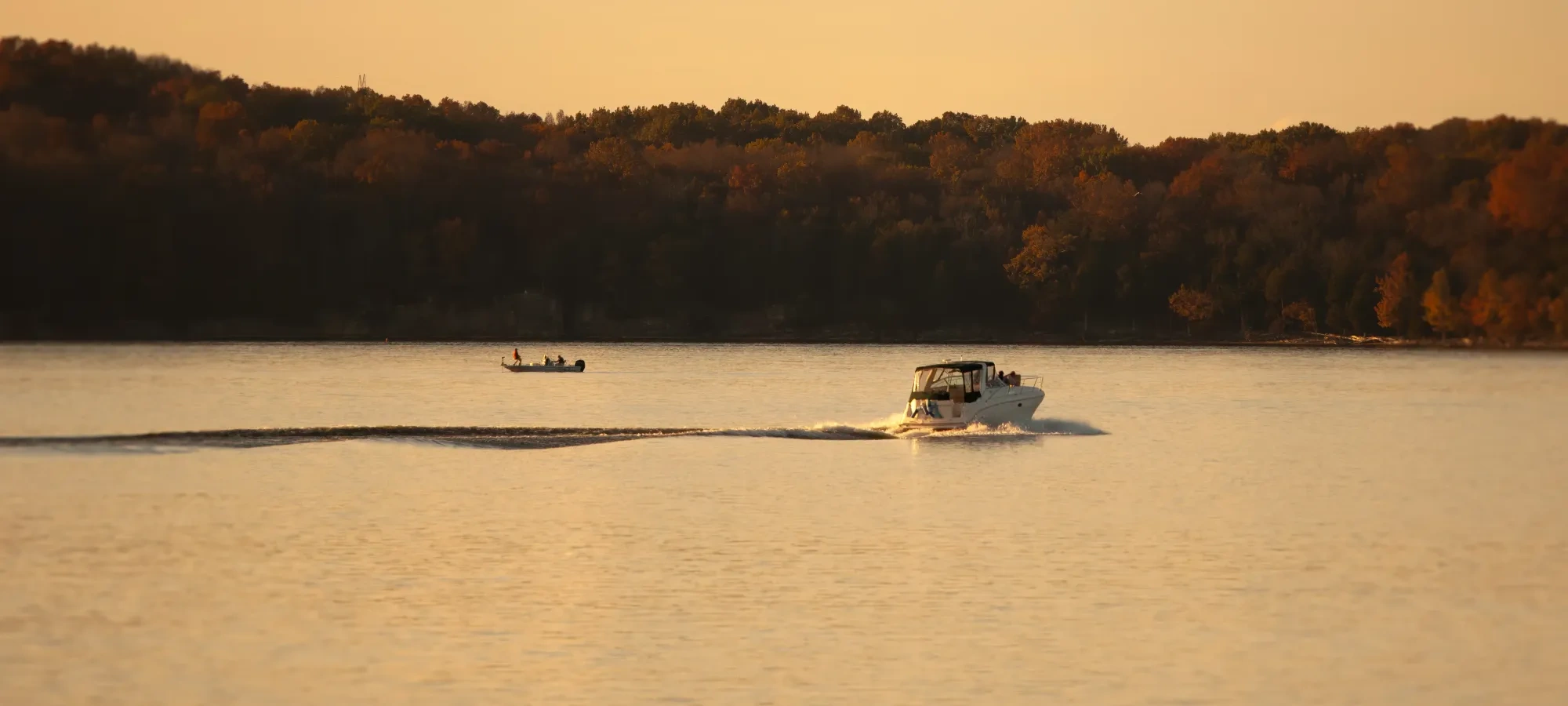 Two boats cruise along the calm waters of a lake at sunset