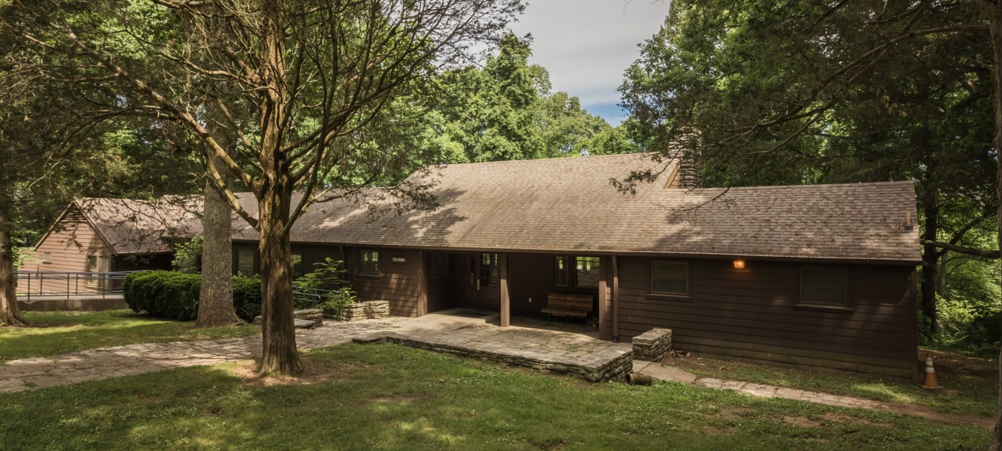 Thatched-roof house surrounded by lush green trees in daylight.