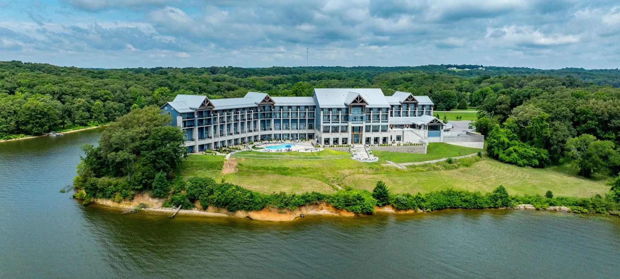 Aerial view of a large hotel by a lake surrounded by greenery.