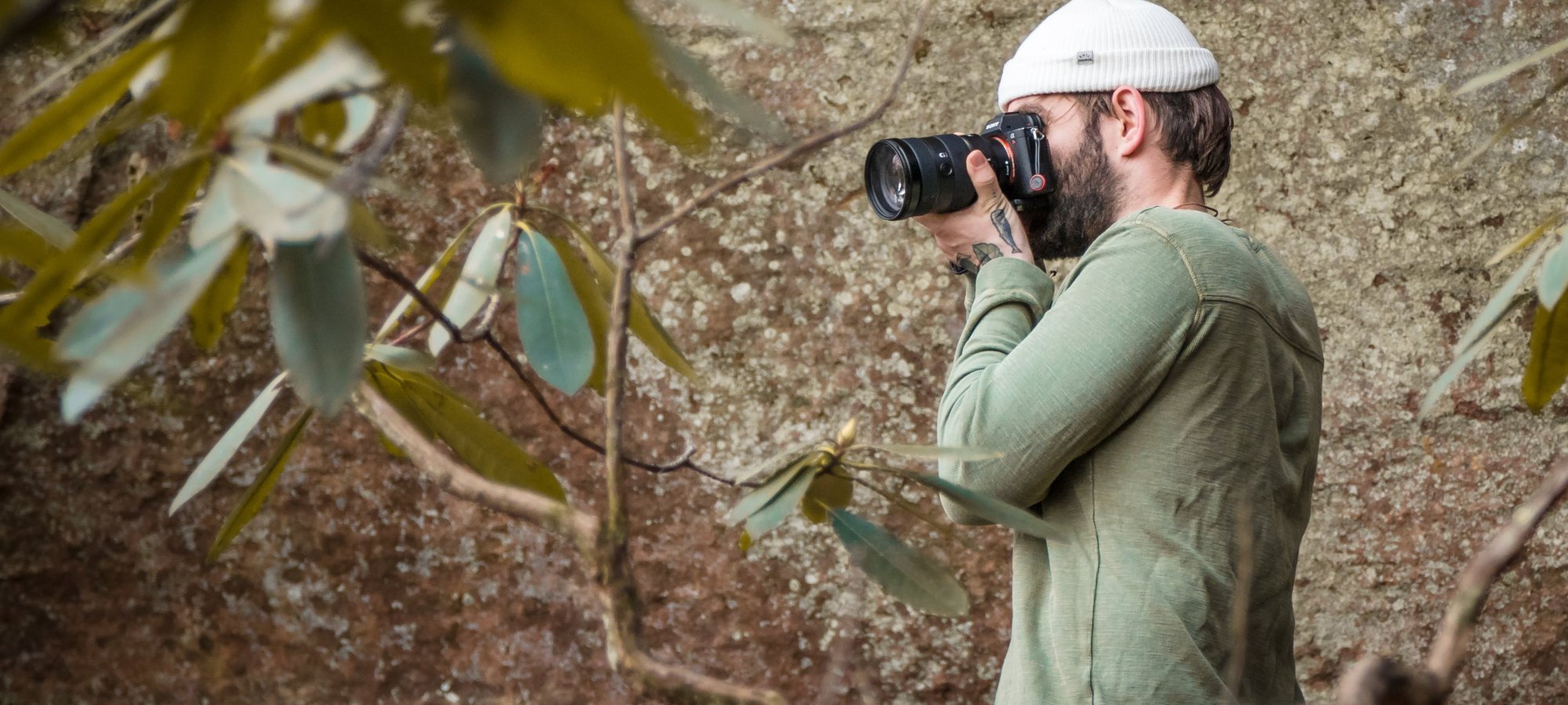 Man in helmet and green shirt using binoculars outdoors.