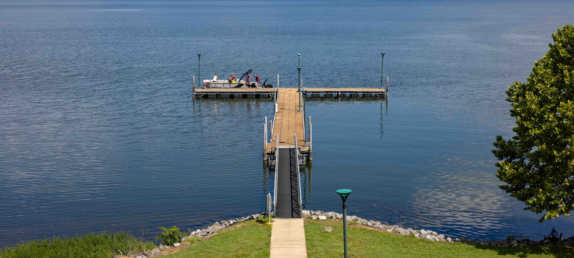 Concrete path leading to a narrow pier on a lake, with people sitting at the end.