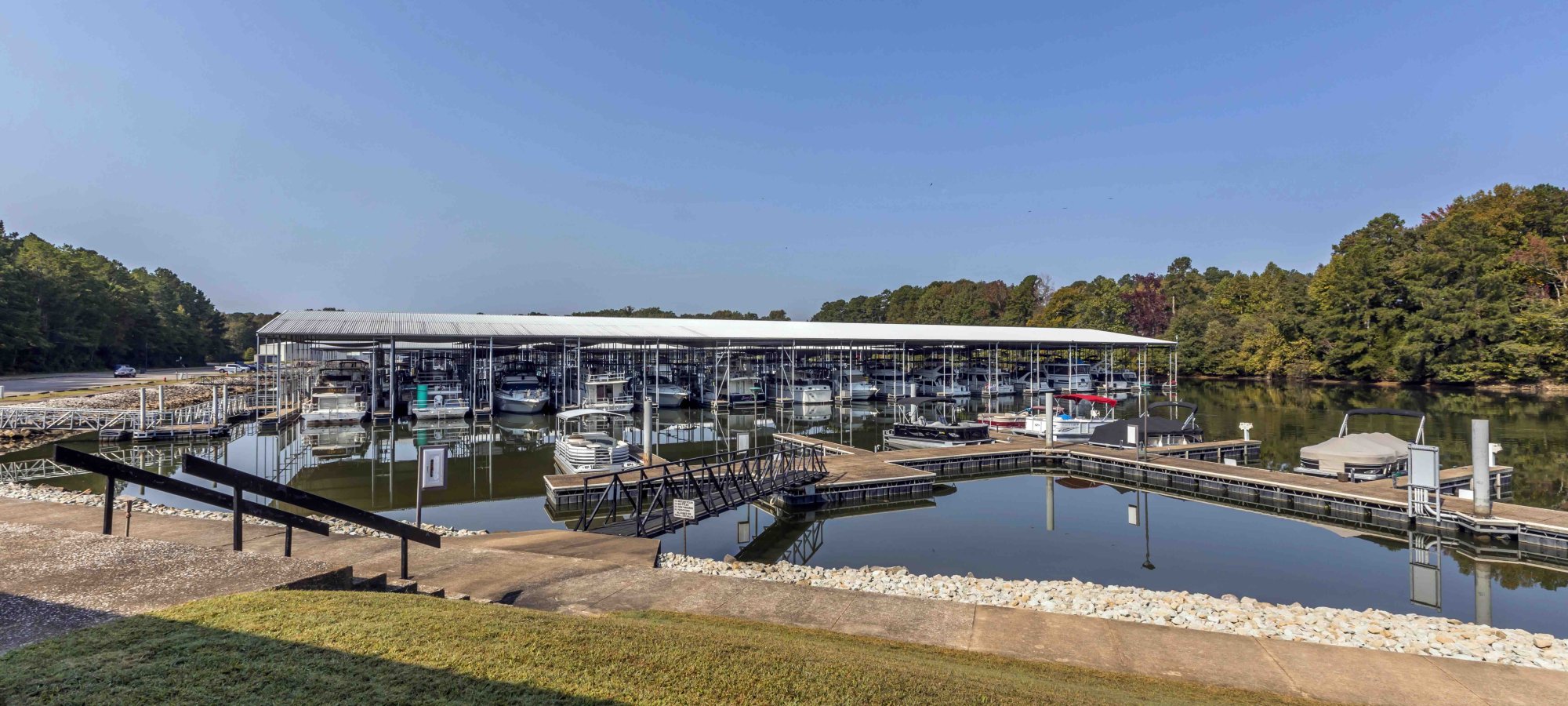Marina with covered boat docks on a calm lake, surrounded by trees.