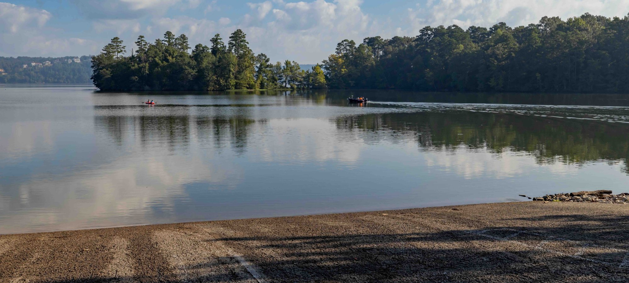 Tranquil lake view with shadows on shore under a cloudy sky.