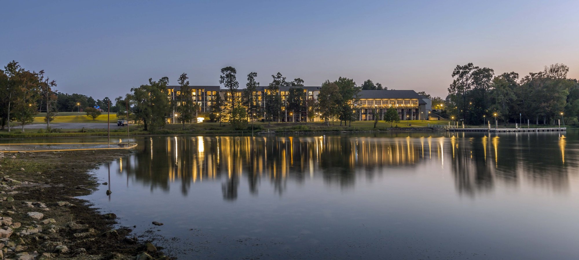 Twilight scene of a calm lake reflecting buildings and trees.