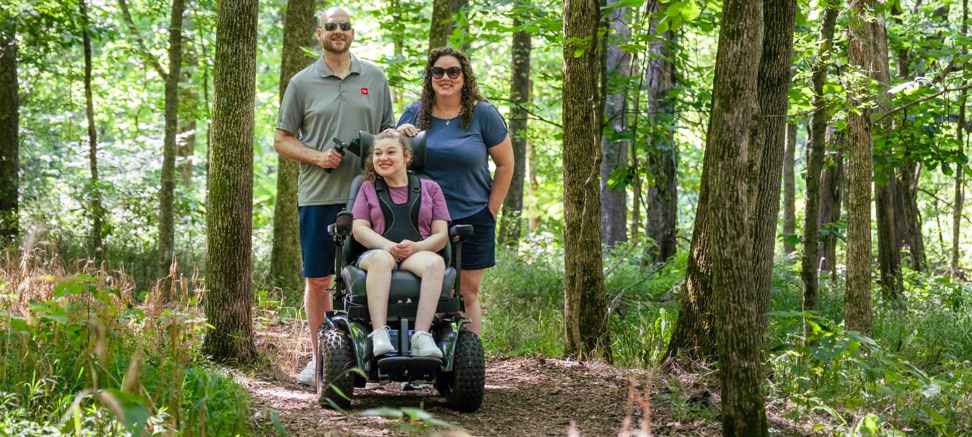Family with a child in a wheelchair on a forest trail.