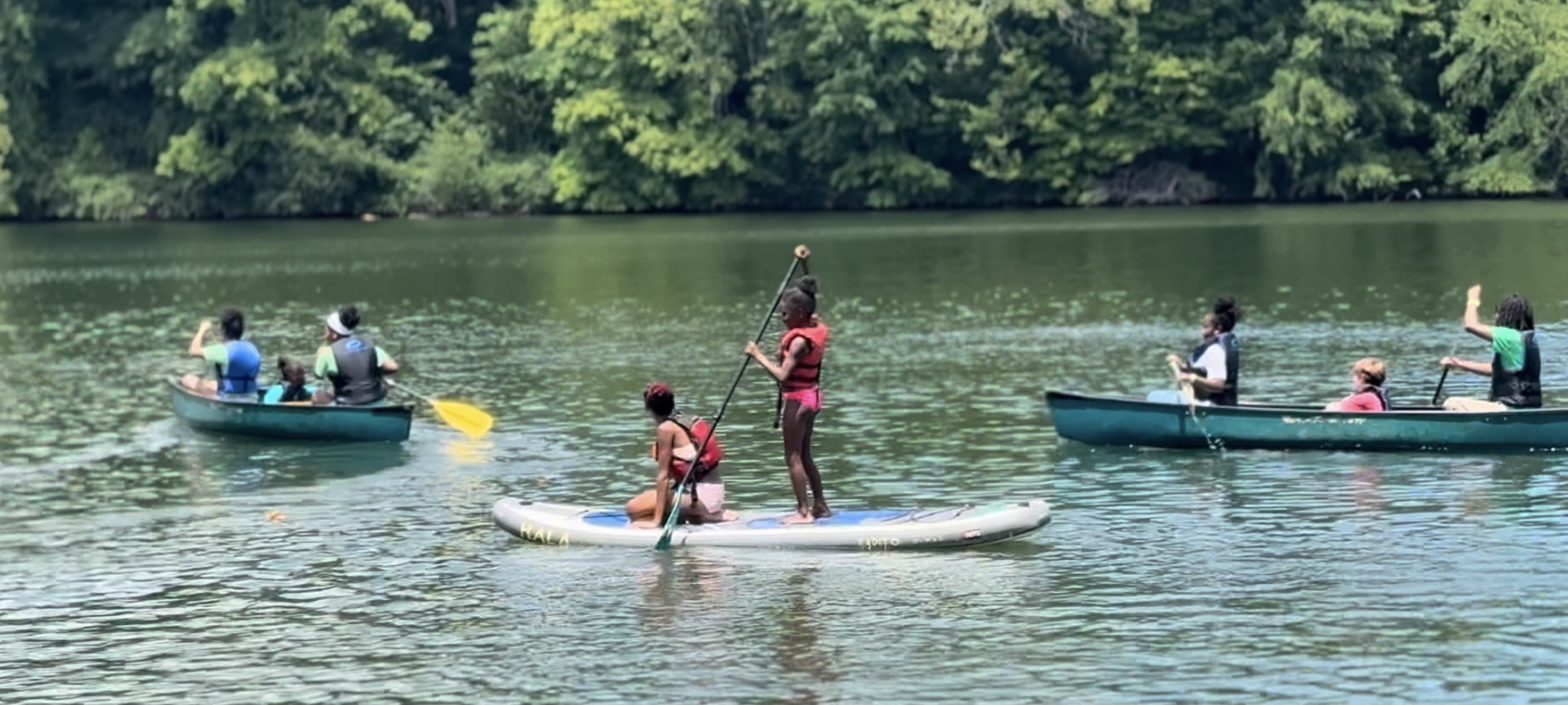 People paddleboarding and canoeing on a lake, surrounded by lush greenery.