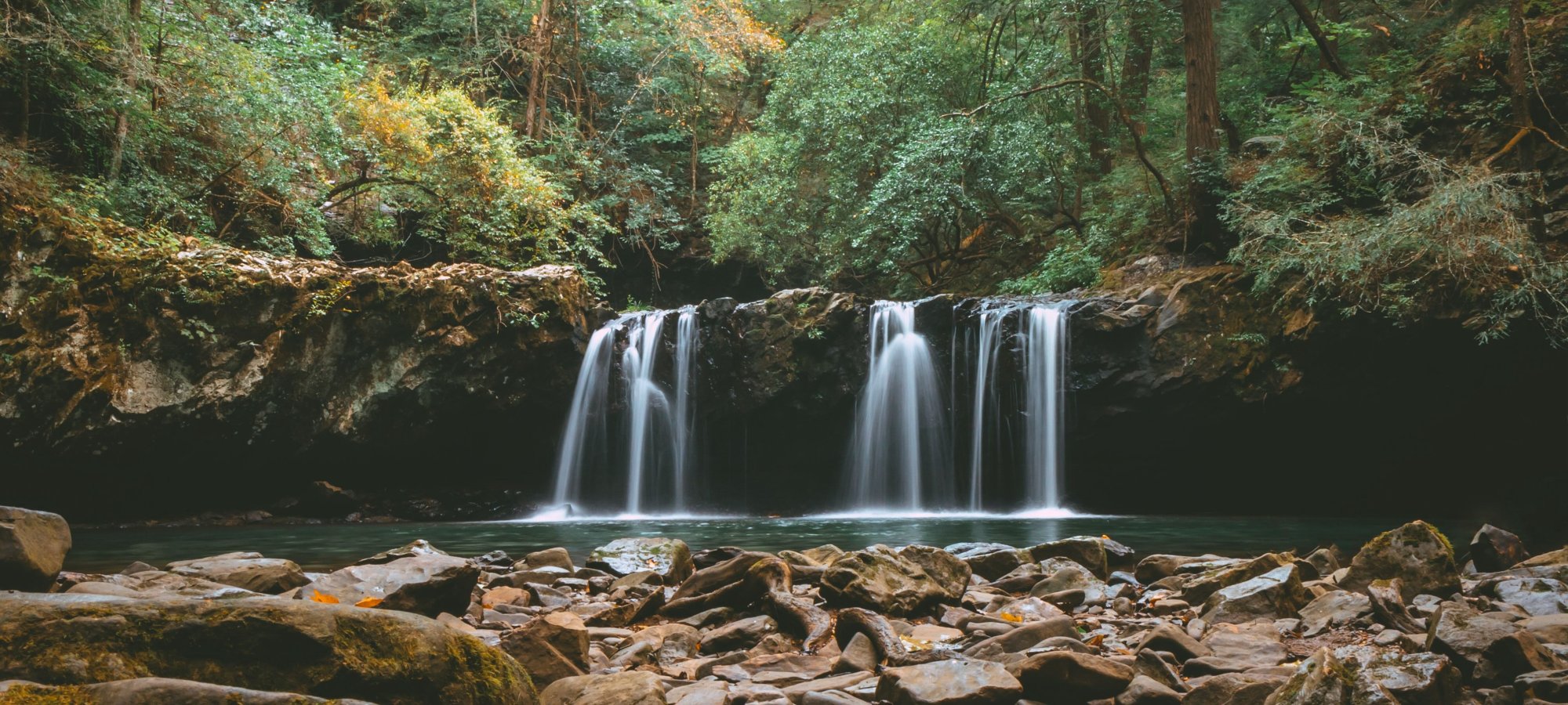 Tranquil waterfall with rocky foreground in a lush forest.