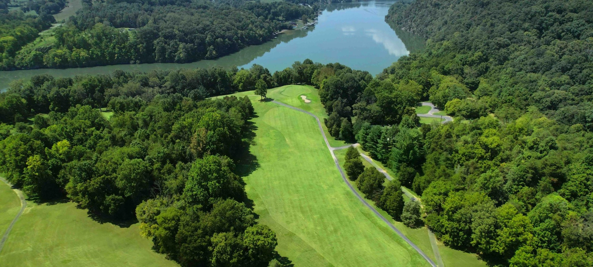 A vibrant green golf course lined with trees that leads up to a lake