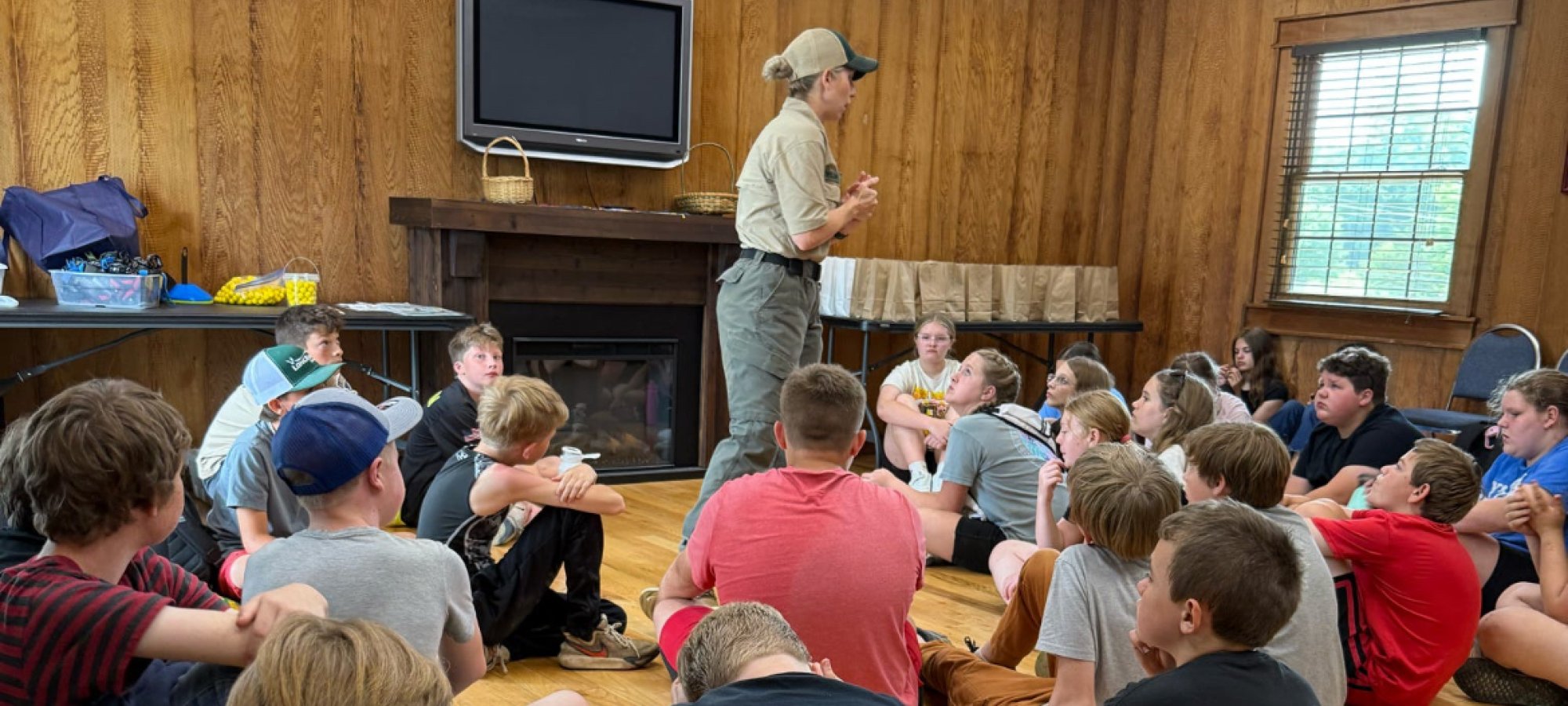 Ranger speaking to a group of attentive children sitting on the floor indoors.
