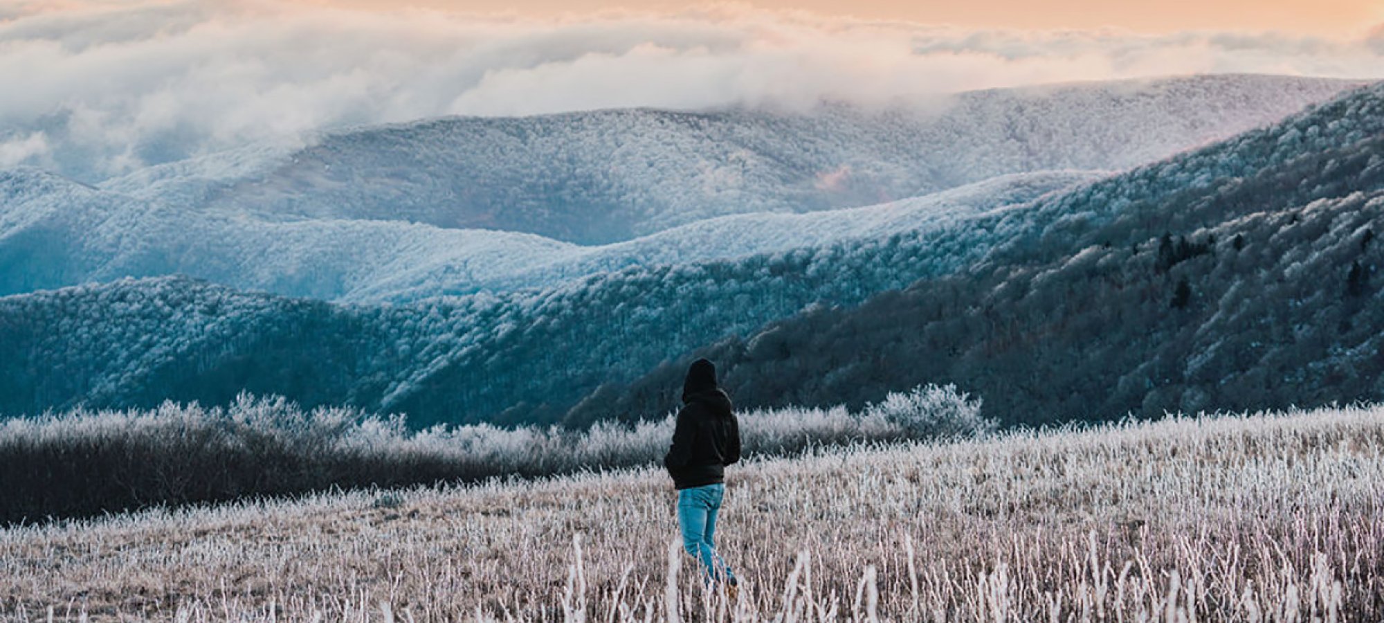 person in the middle of a field in the winter looking out onto mountains