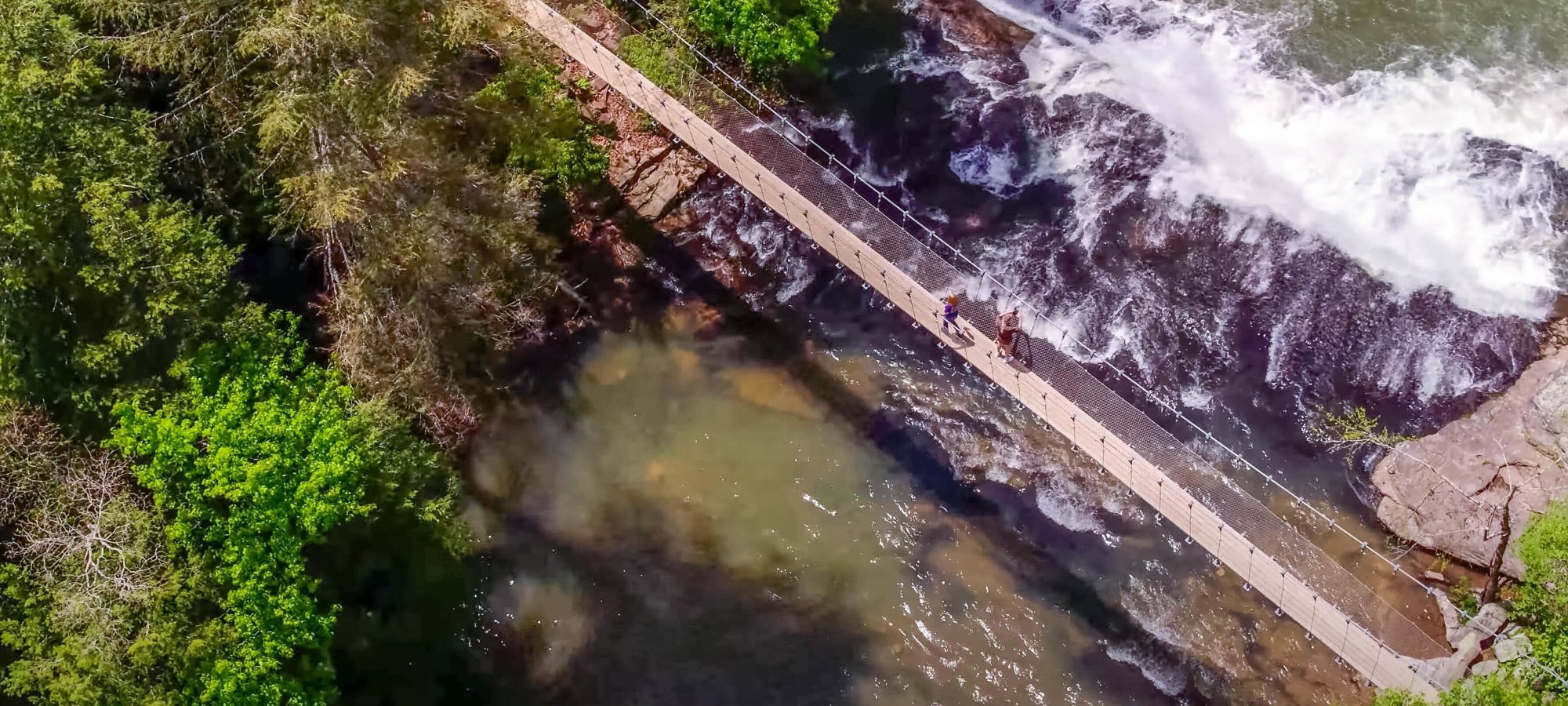 Aerial view of a thin bridge next to a waterfall.