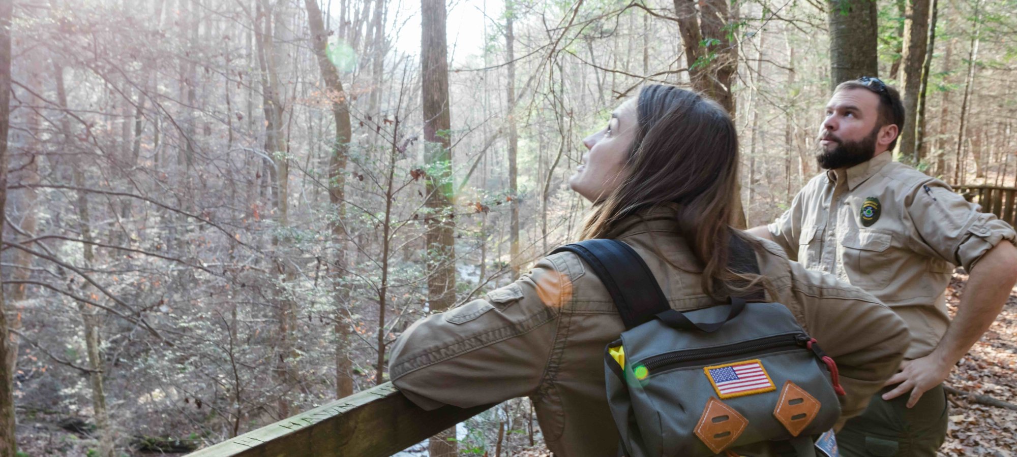 Two park rangers observing nature from a wooden bridge.