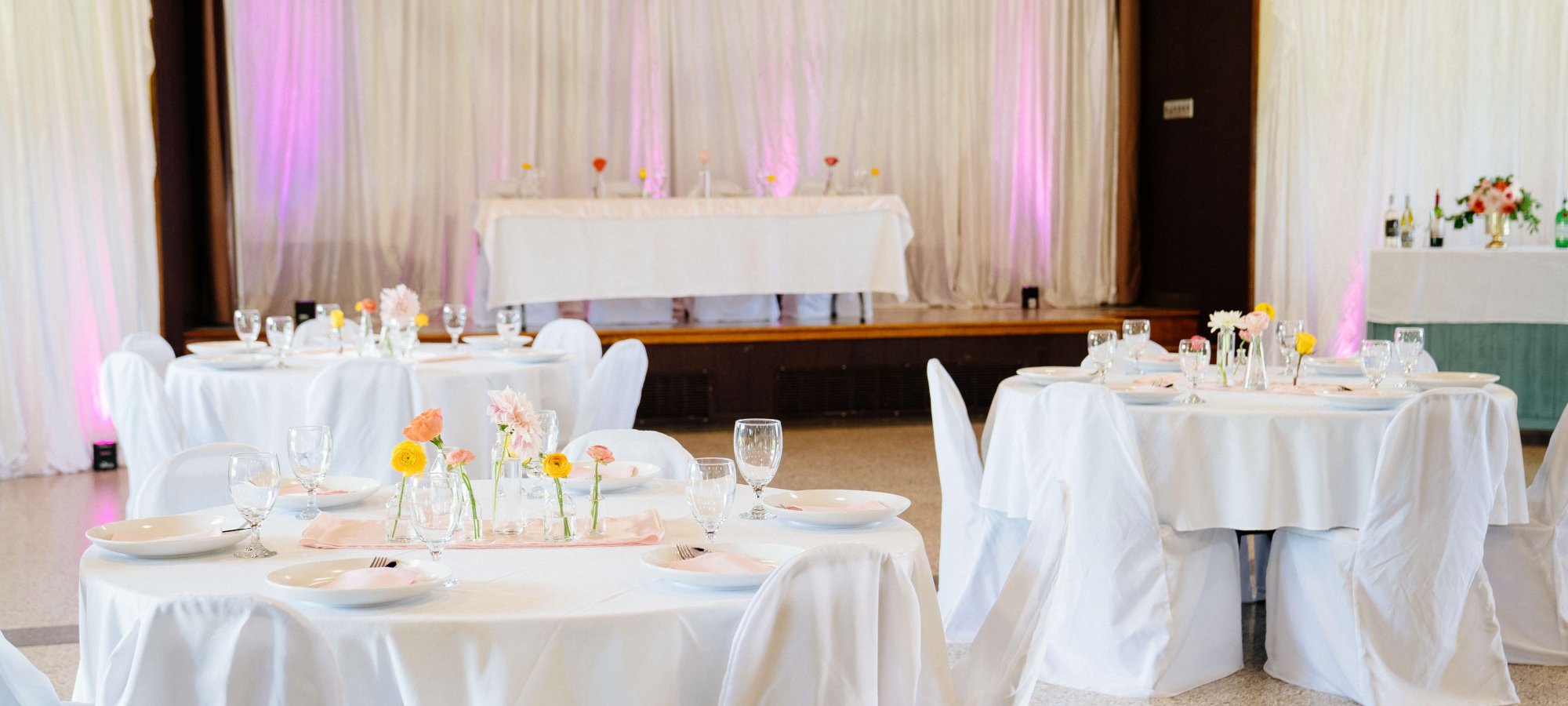 Elegant wedding reception hall decorated with white tablecloths and pink lighting.