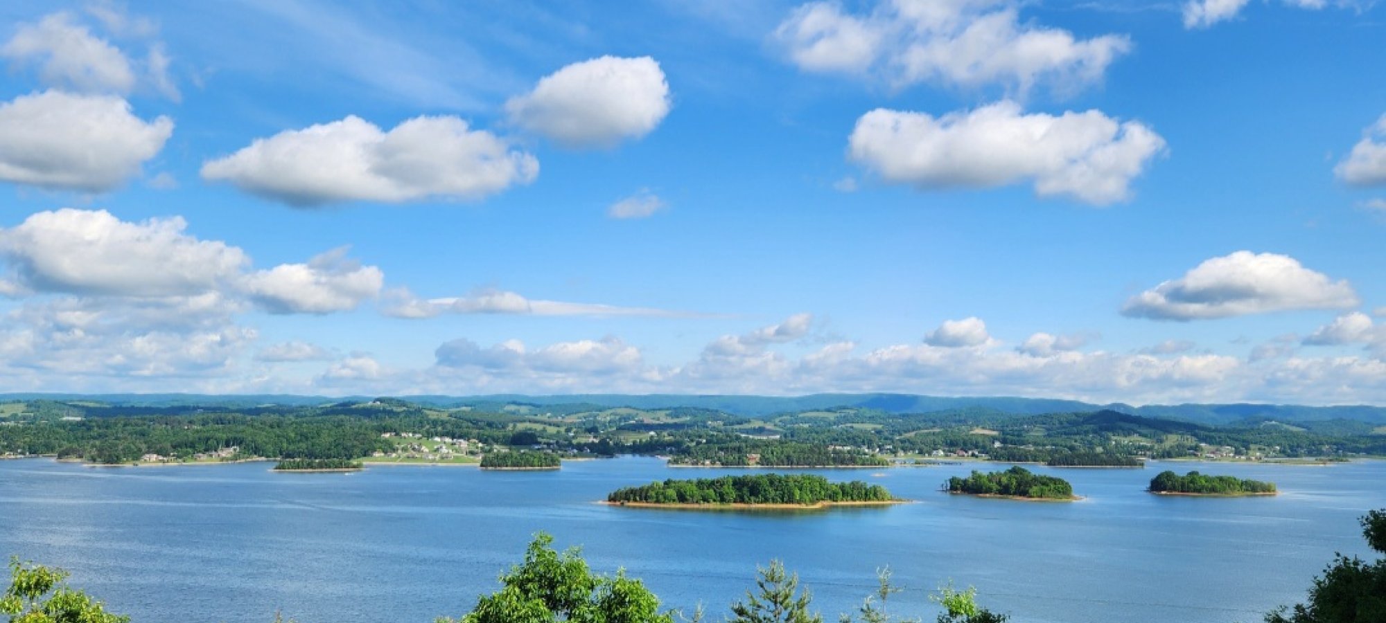 Scenic view of a large lake with islands, fluffy clouds, and blue skies.