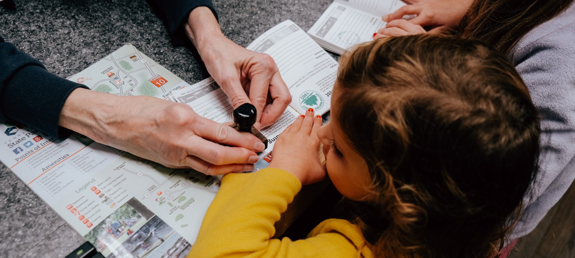 Adults and a young girl with a map and magnifying glass on a table.