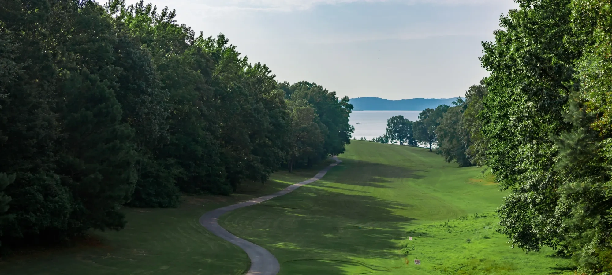 A green golf course rolling down a hill with a lake in the distance