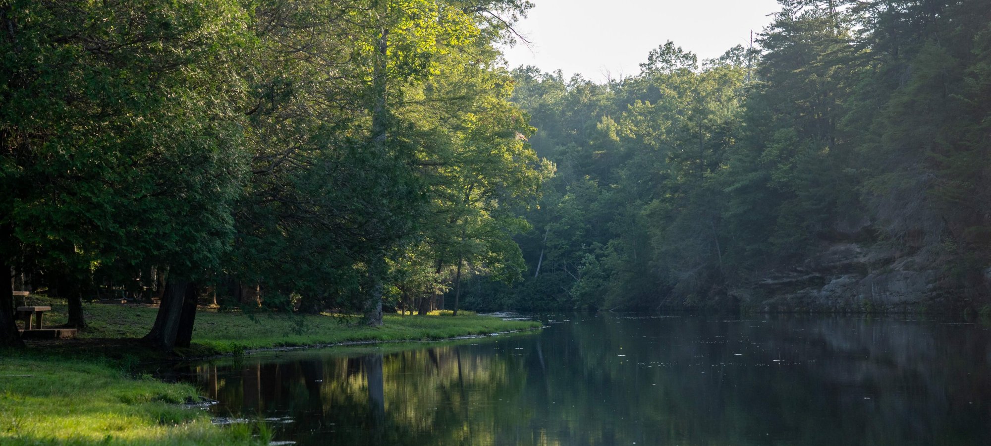 Serene river with lush trees on its bank in early morning light.