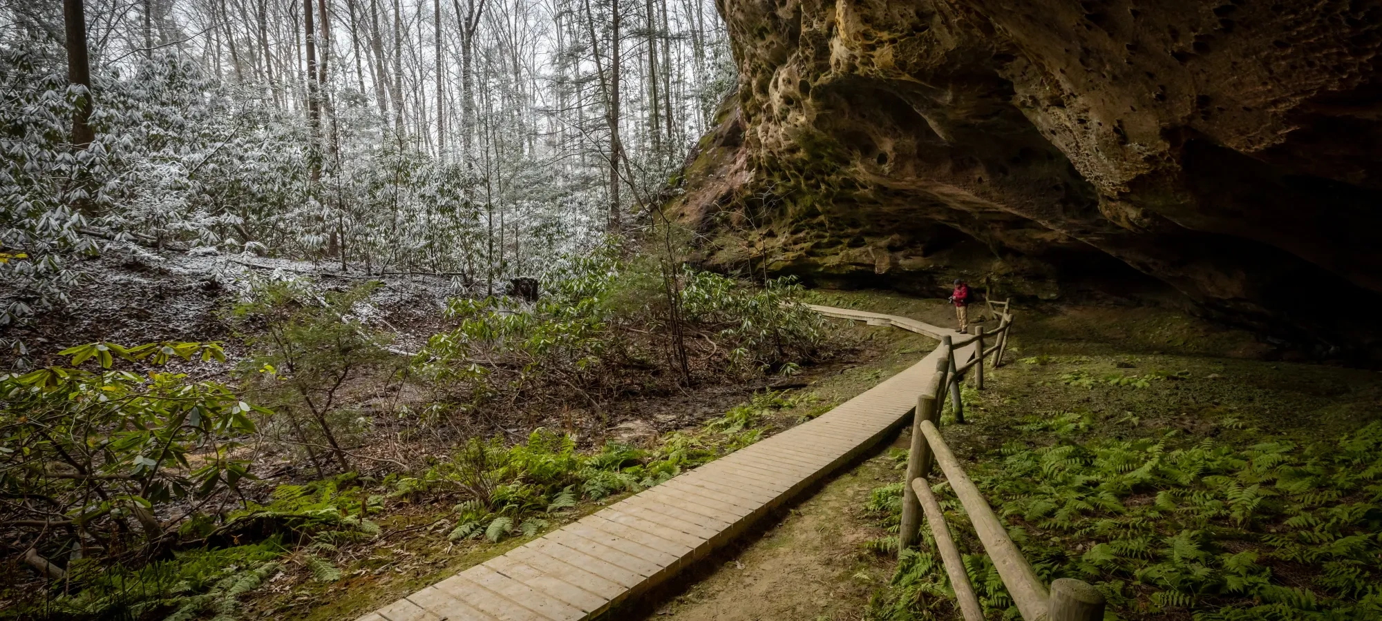A large rock house extends over a wooden boardwalk surrounded by snowy trees