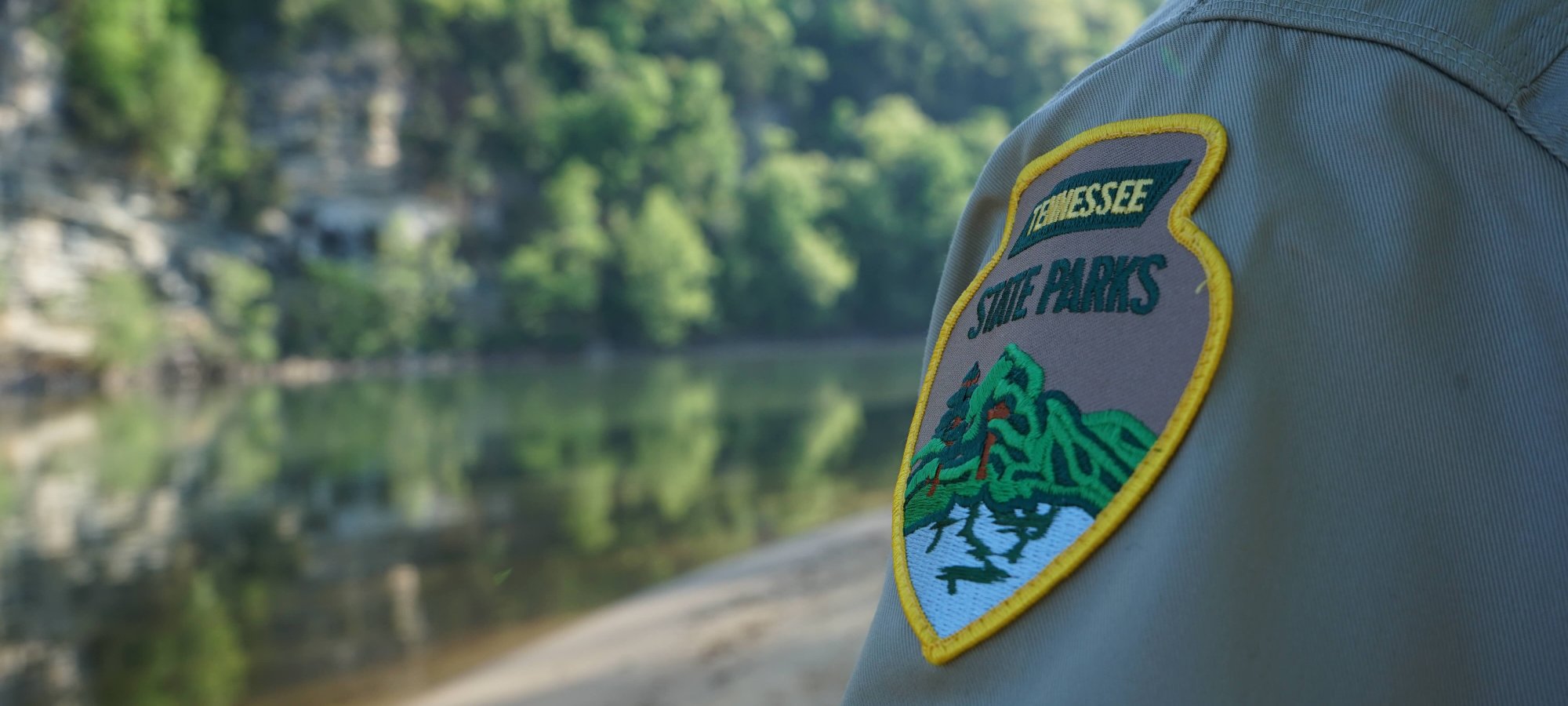Park ranger's shoulder patch with a tranquil river landscape in the background.