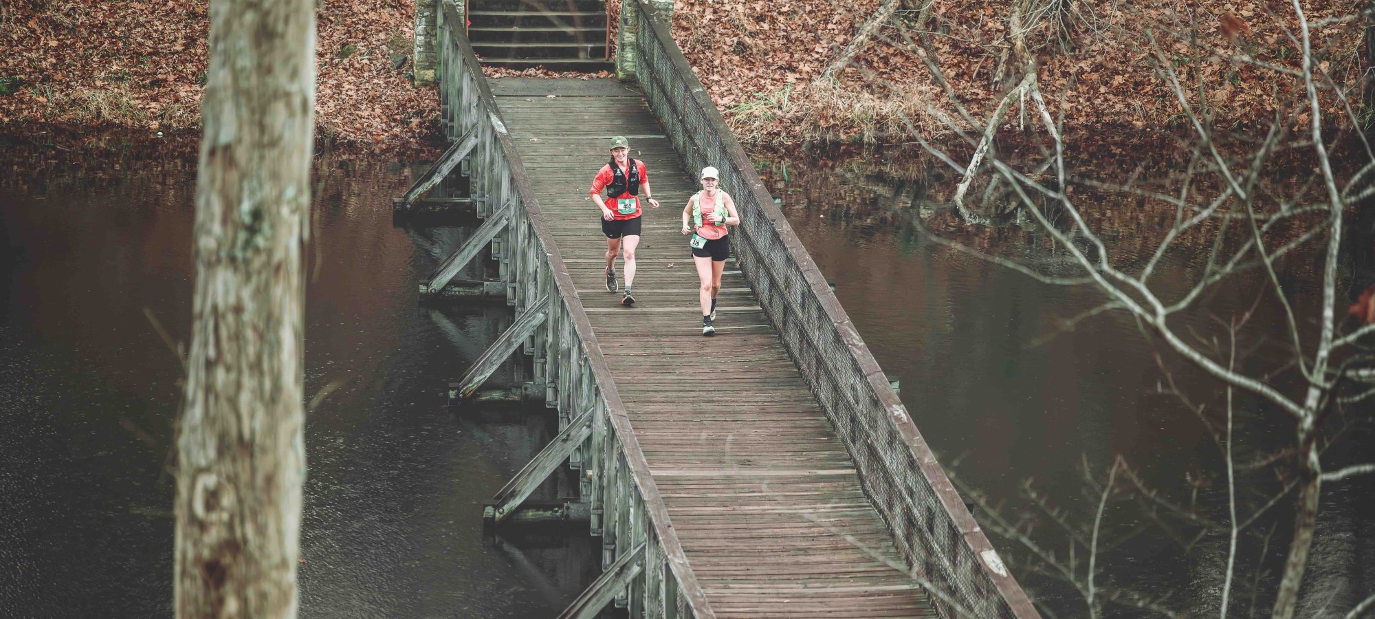 two runners running on a wooden bridge over some water.