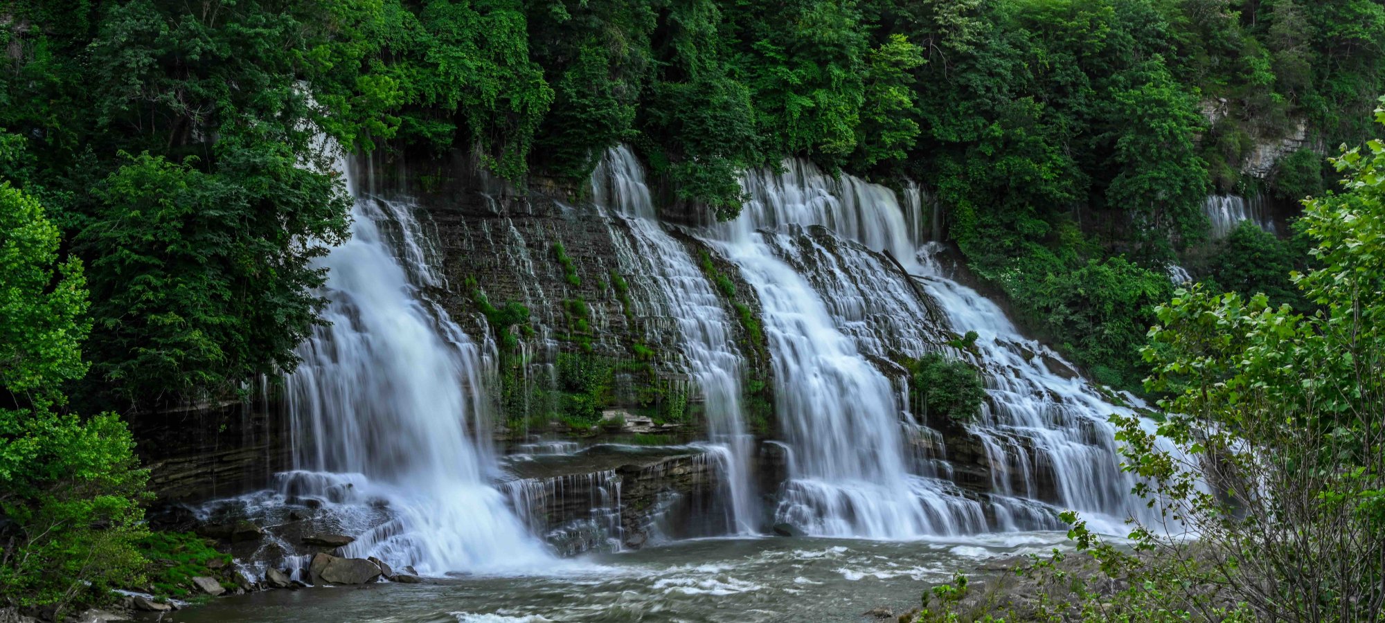Lush waterfall cascading over rocks surrounded by green trees.