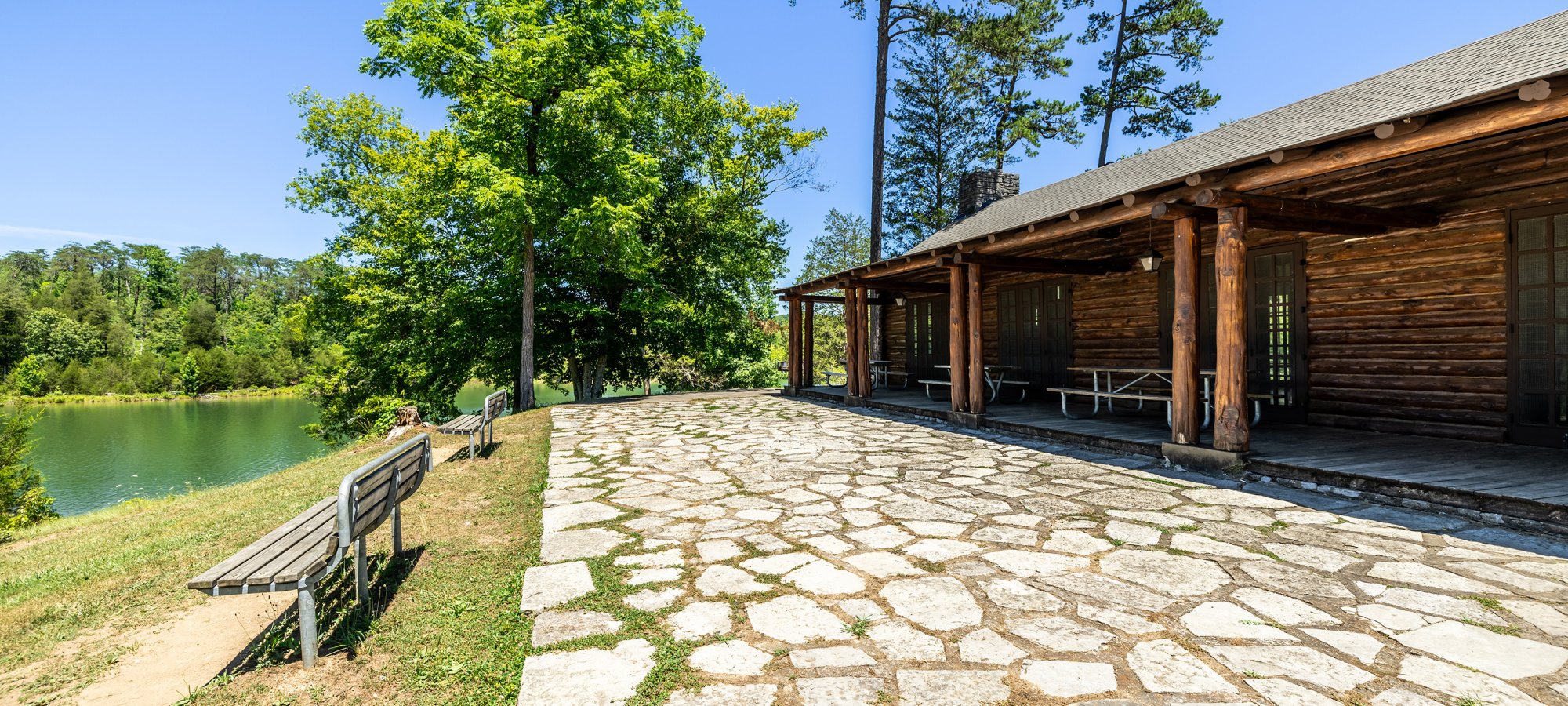 Stone pathway leading to a lakeside cabin with benches under trees.