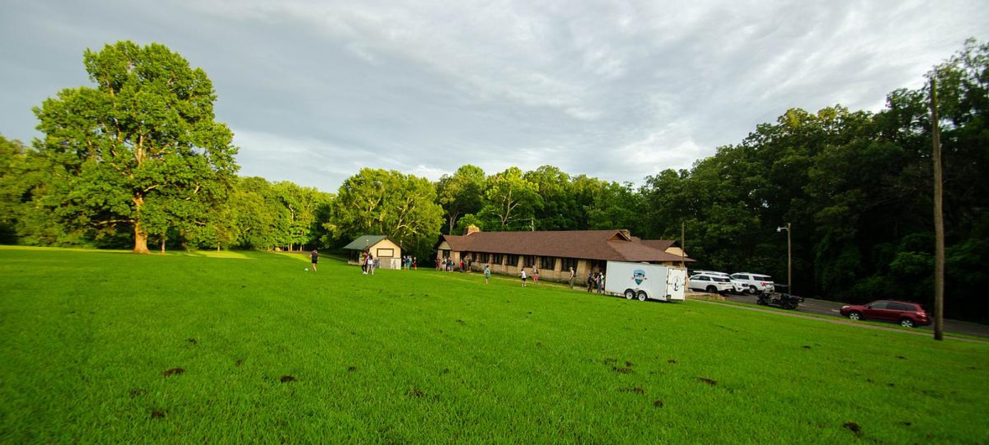 A grassy field with a Group Camp Mess Hall in the background, surrounded by trees.