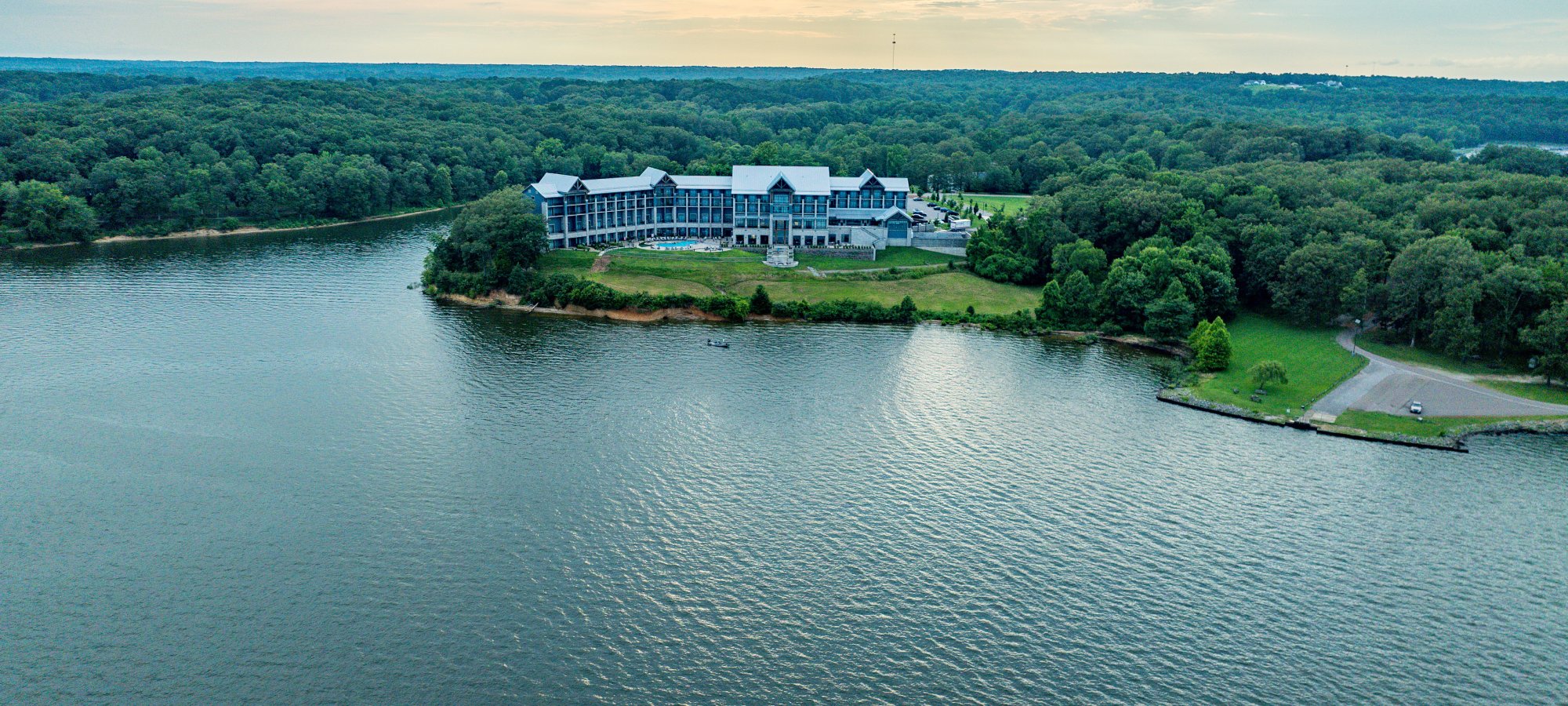 Aerial view of a lakeside lodge surrounded by trees under a cloudy sky.