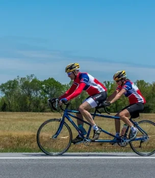 Two cyclists on a tandem bike in a rural area under a clear blue sky.