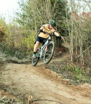 Cyclist jumping on a dirt trail in a wooded area.