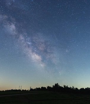 starry night sky making a line in the sky with trees in the distance