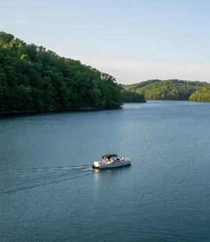 Boat cruising across a calm lake surrounded by forested hills.
