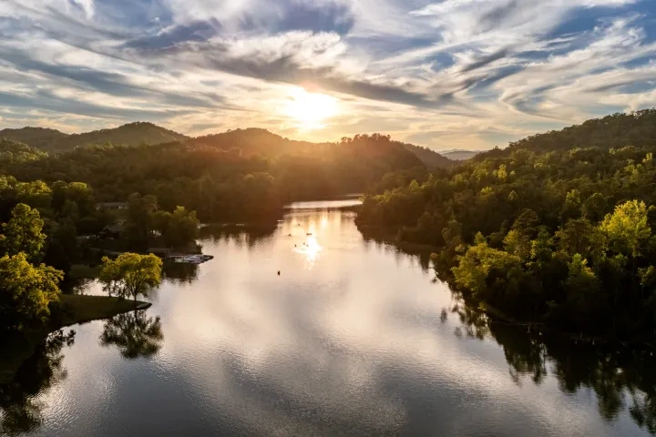 Sunset over a tranquil lake surrounded by lush green hills and dramatic clouds.