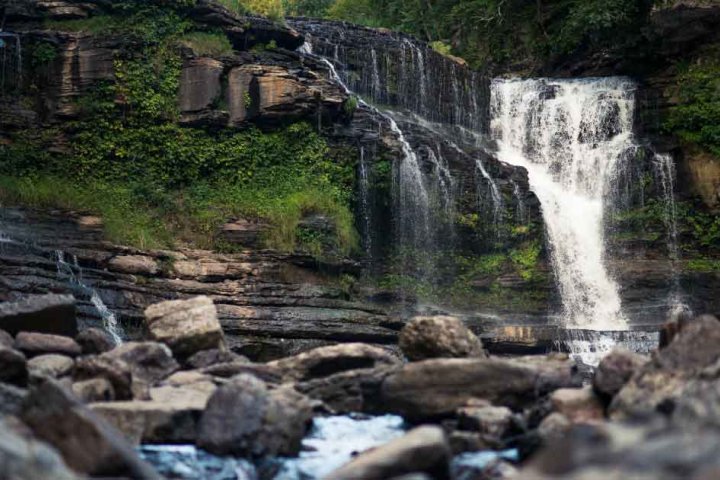 Waterfall cascading over rocky cliff into a boulder-strewn river.
