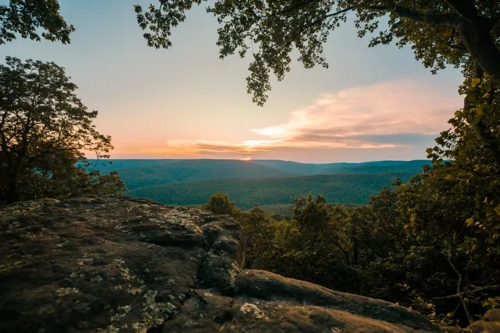 Sunset over a forested valley viewed from a rocky overlook.