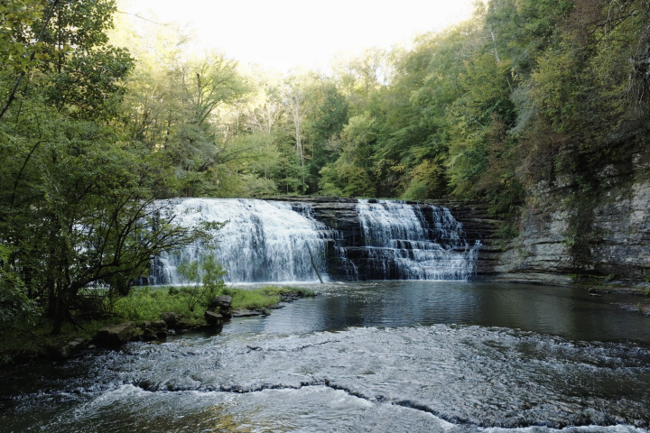 A cascading waterfall drops into a shallow pool surrounded by green trees