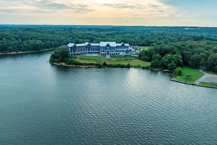 Aerial view of a lakeside lodge surrounded by trees under a cloudy sky.