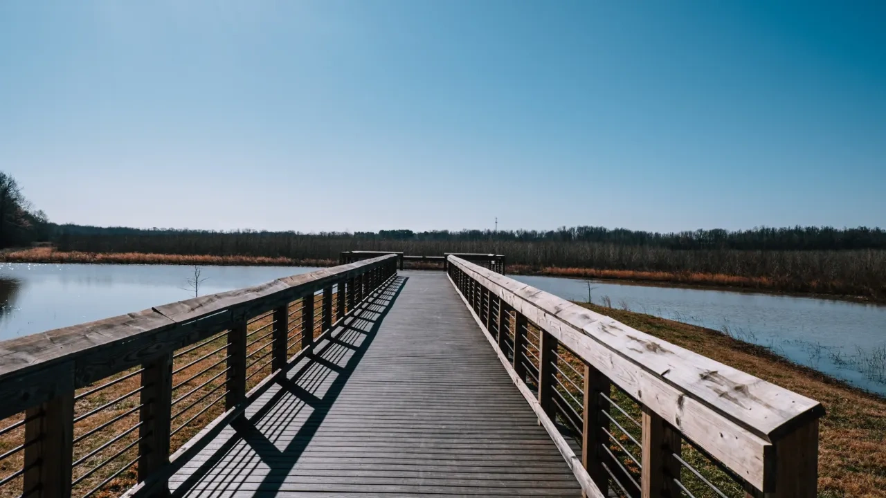 Wooden boardwalk over a river under a clear blue sky.