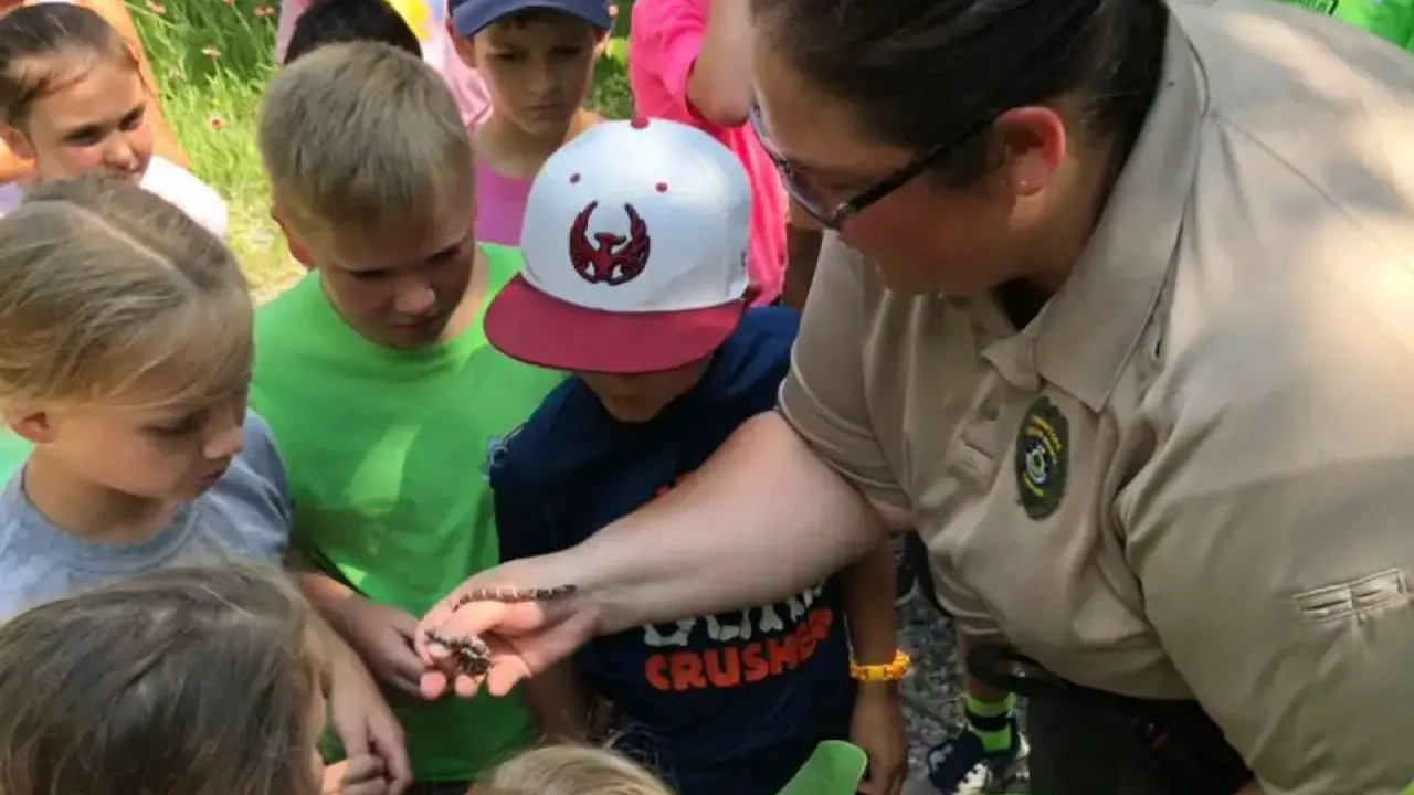 Park ranger showing kids a small snake in a forest setting.