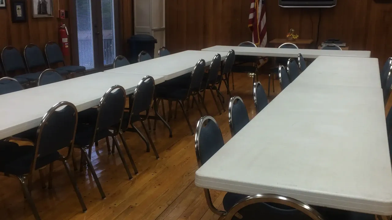 Meeting room with tables, chairs, wooden floor, and American flag.