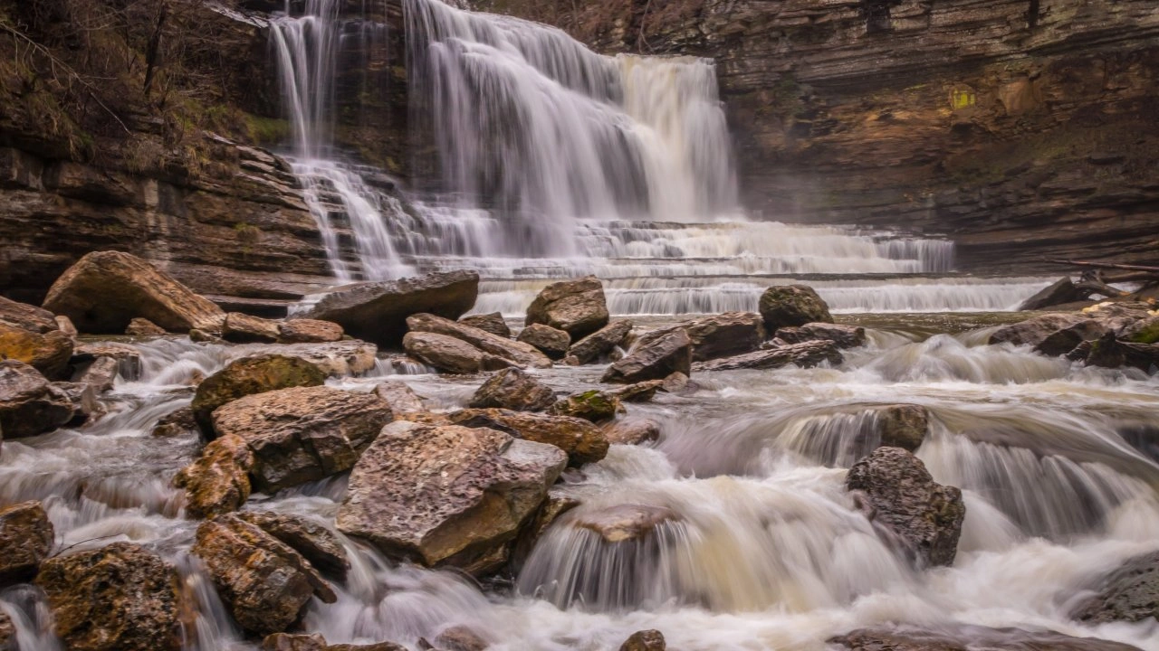 Waterfall cascading over rocky ledges with surrounding cliffs.