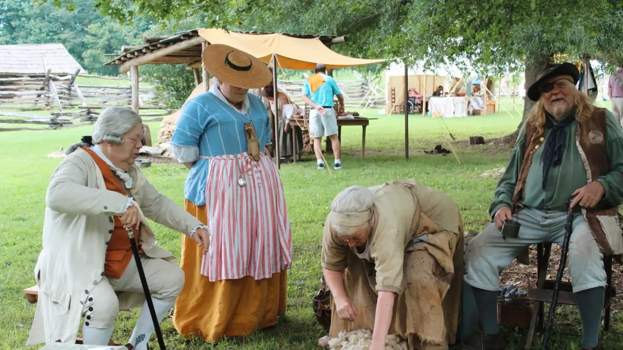 People in historical attire at a reenactment event under trees.