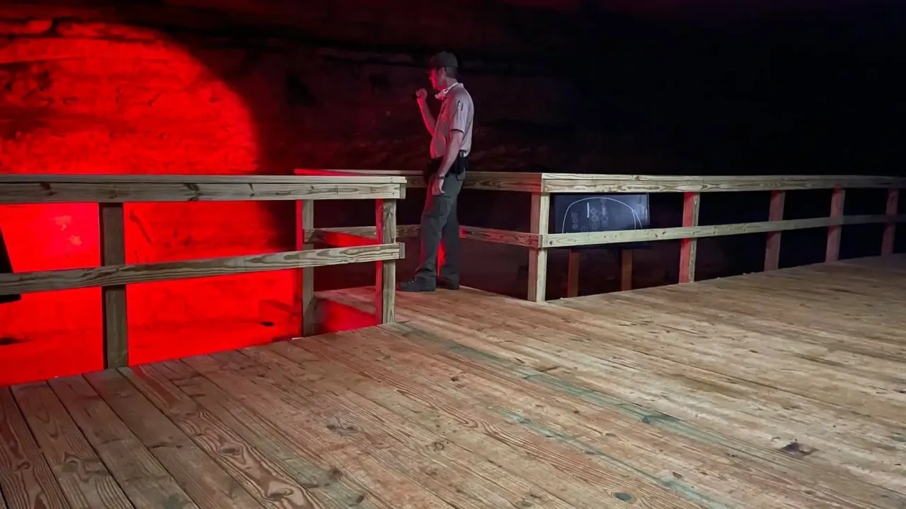 Man with flashlight on wooden platform, red-lit background.