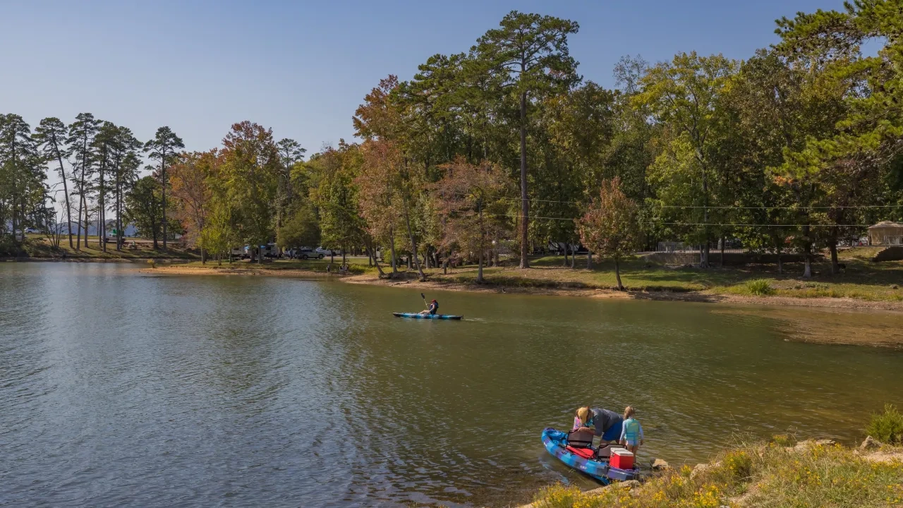 People kayaking on a calm lake surrounded by trees under a clear blue sky.